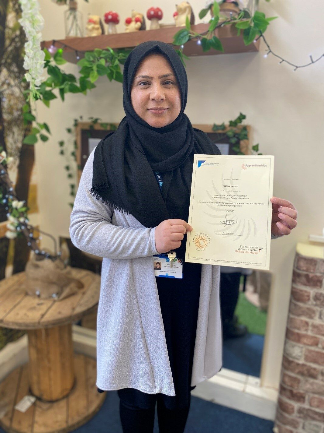 A lady in a headscarf holding a certificate and smiling
